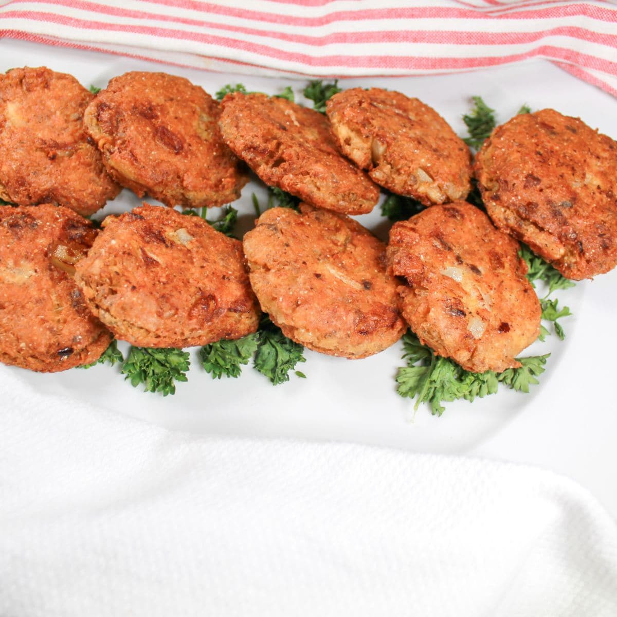 Salmon patties on a white plate with some greenery. A pink and white stripped dish towel next to the plate.