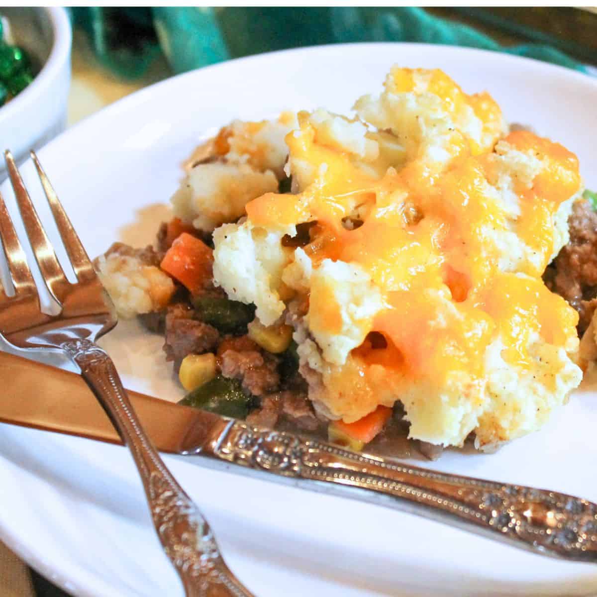 Shepherd's pie on a white plate with a fork and knife.