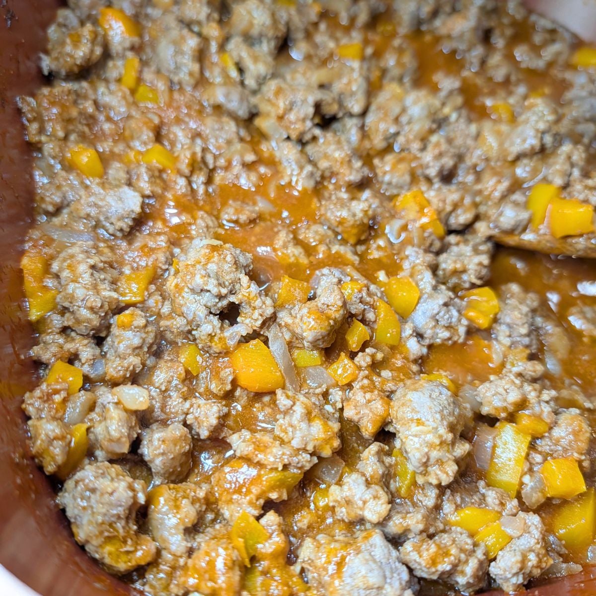 Adding sloppy joe sauce to the meat and vegetables in a skillet.