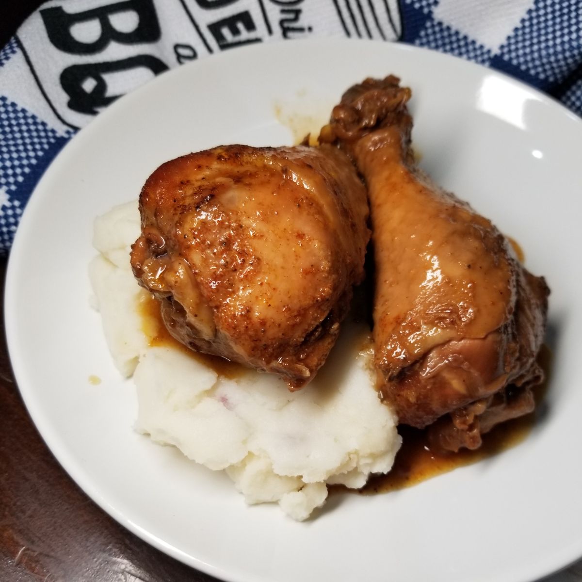 Cooked chicken legs sitting on top of mashed potatoes in a white serving bowl.