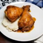 BBQ chicken legs sitting on top of mashed potatoes in a white serving bowl.