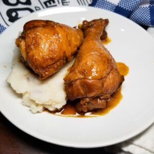BBQ chicken legs sitting on top of mashed potatoes in a white serving bowl.