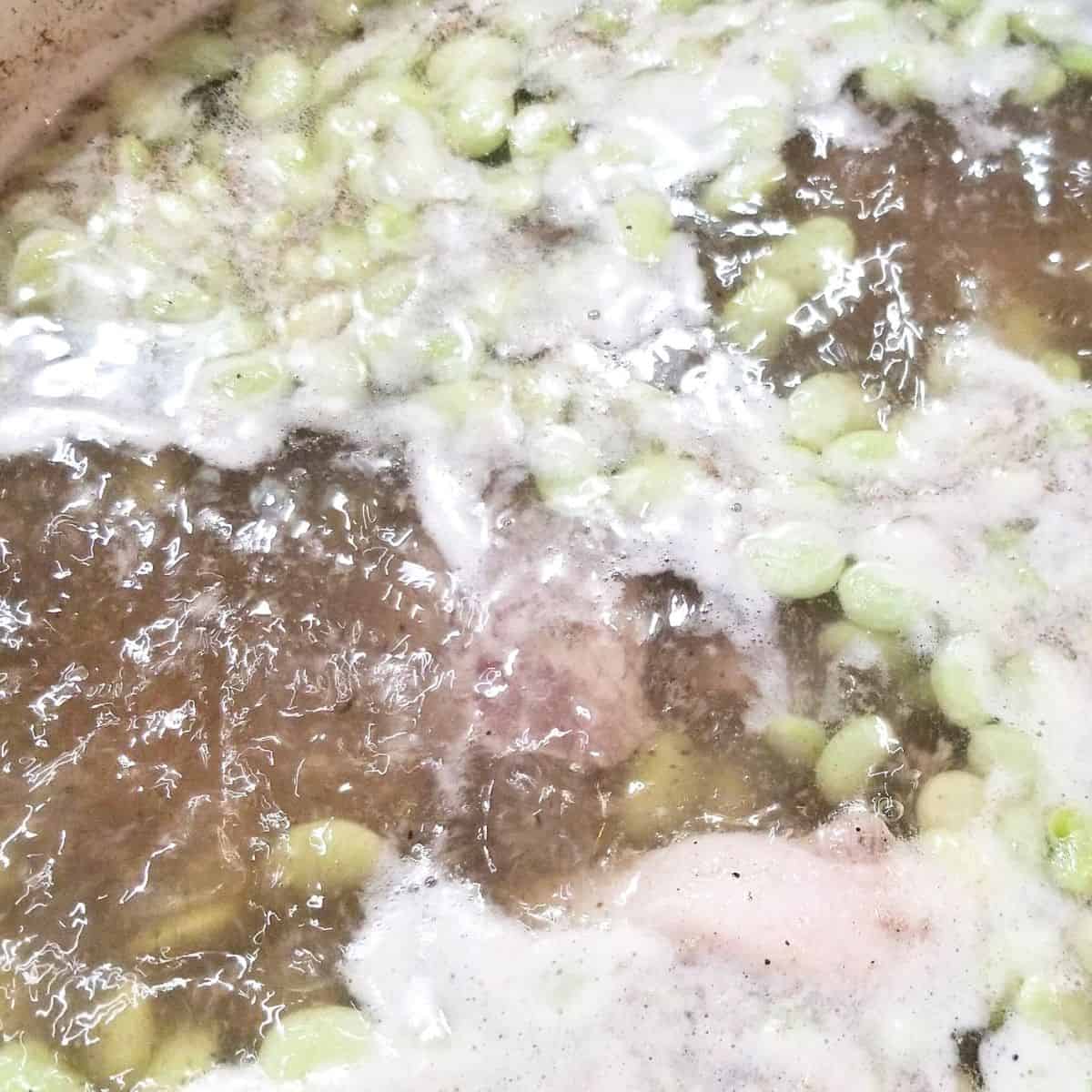 Southern lima beans and neckbones boiling in a large pot on stovetop.