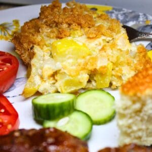 Squash Casserole on a plate with cucumbers, tomatoes, bbq, and cornbread.