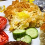 Squash casserole on a plate with cucumbers, tomatoes, cornbread, and bbq.