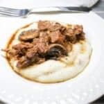 Garlic Butter Steak Bites over mashed potatoes in a white bowl.