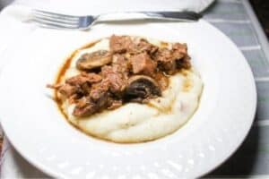 Garlic Butter Steak Bites over mashed potatoes in a white bowl.