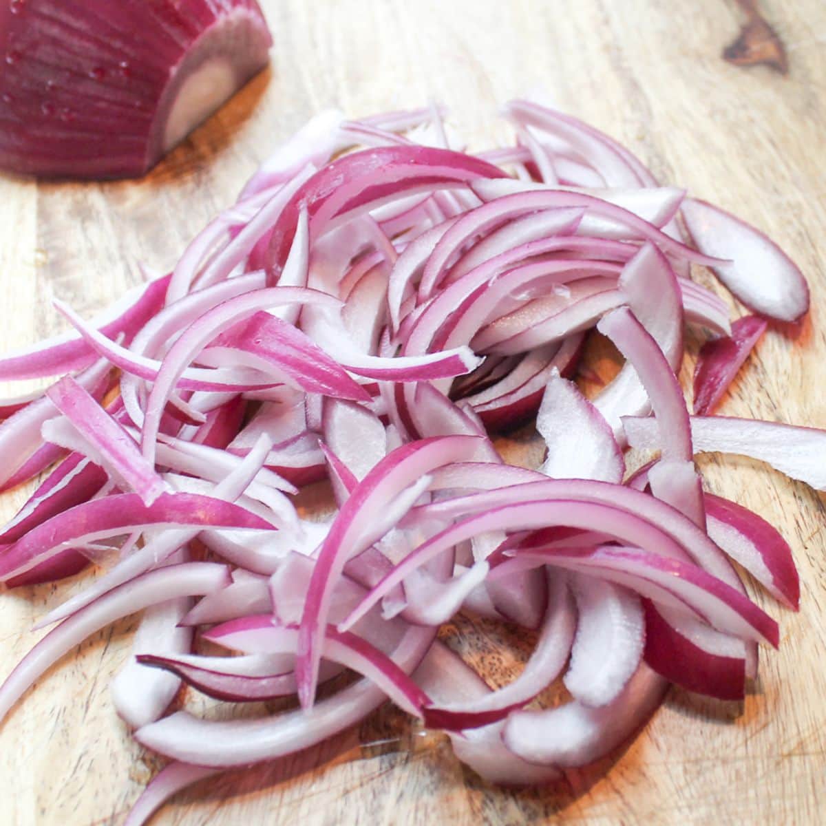 Thinly sliced red onions on a cutting board.