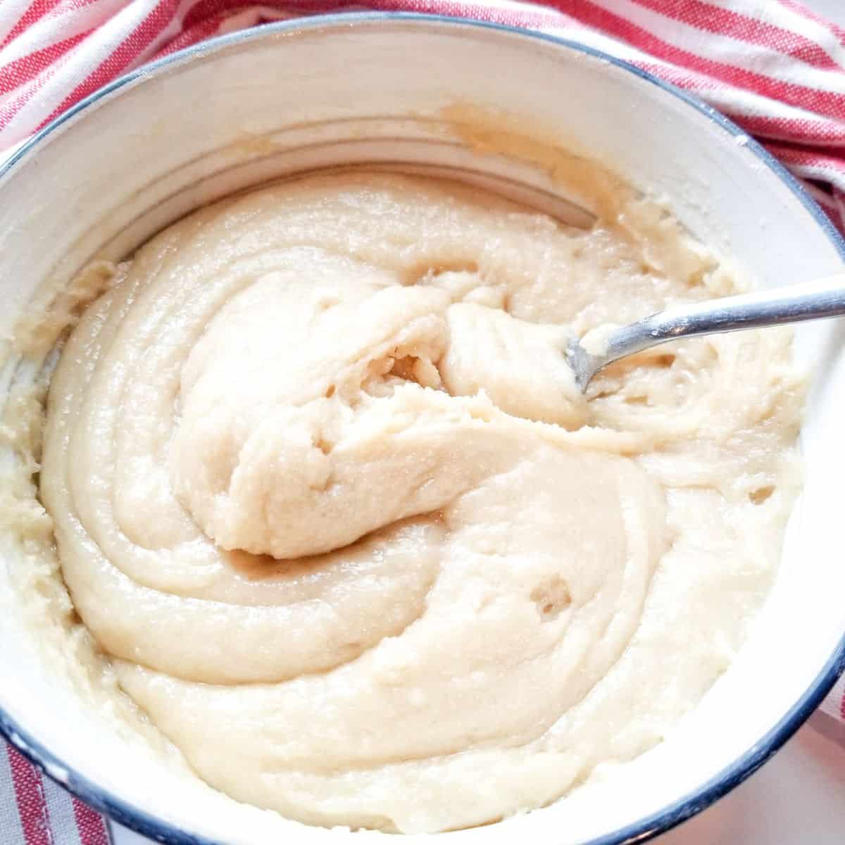 The dough in a blue bowl with a spoon and a red and white dish cloth.