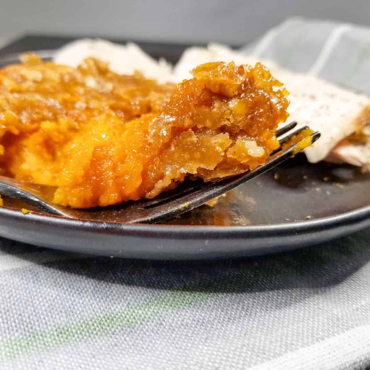 Sweet potato casserole with a fork on a black plate.
