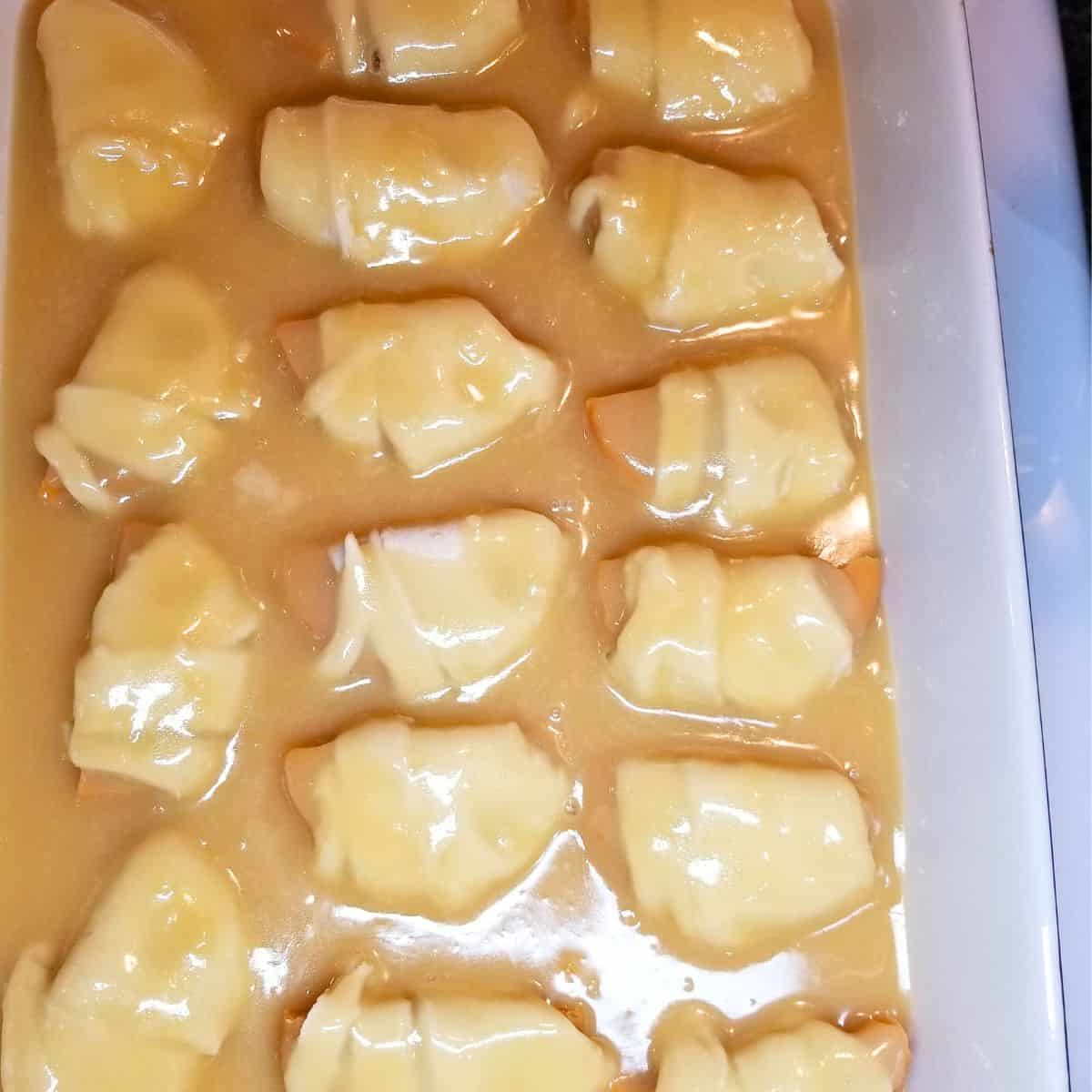 Creamy sauce poured over unbaked sweet potato dumplings in baking dish.