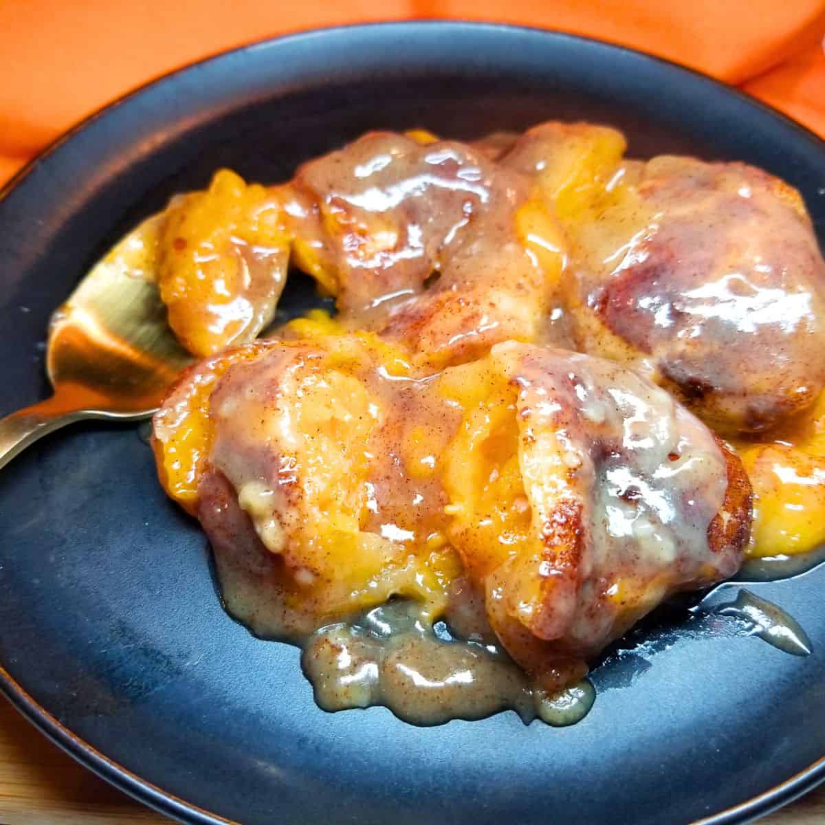 Spoon scooping sweet potato dumplings with sauce onto a dessert plate.