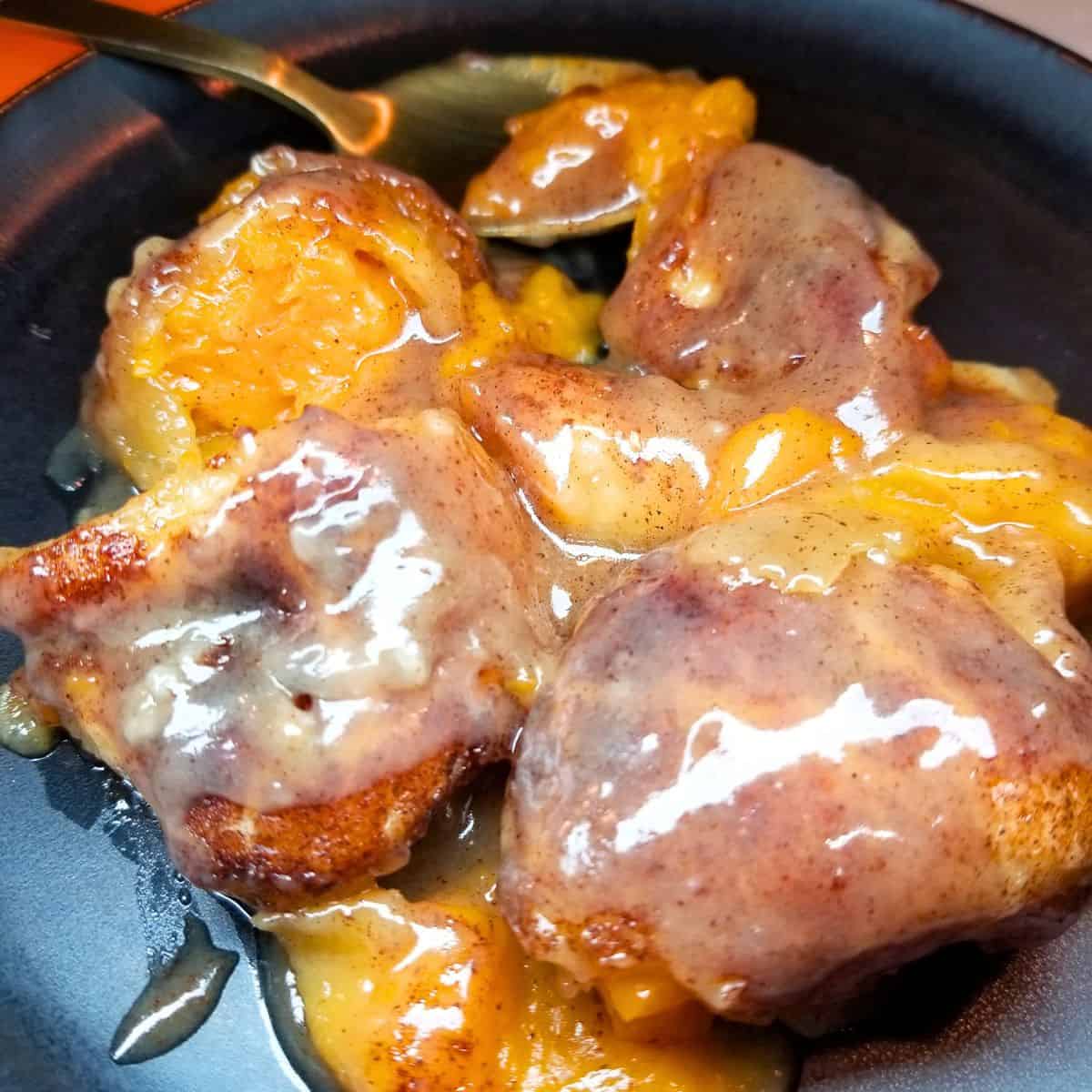 Sweet potato dumplings baked in a cinnamon sauce and served on a black dish with a spoon.
