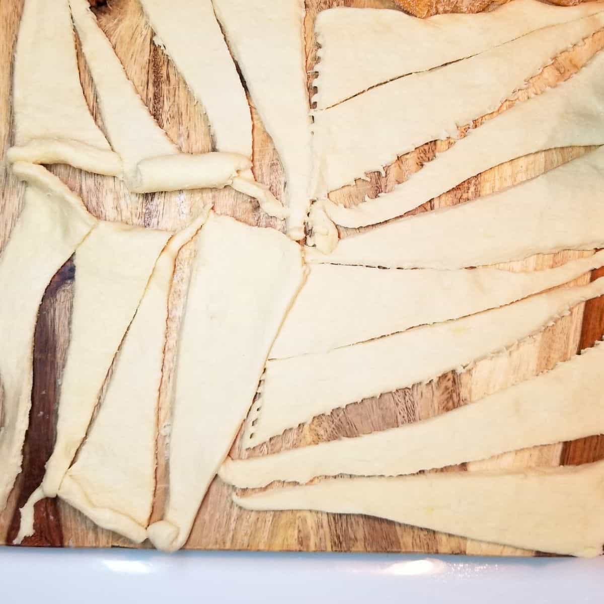 Crescent roll dough triangles cut into long strips for wrapping sweet potatoes.