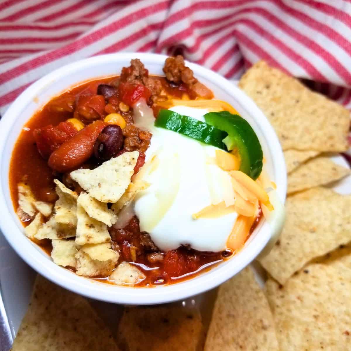 Easy taco soup in a white bowl with sour cream, cheese, and jalapenos. Tortilla chips on the side.