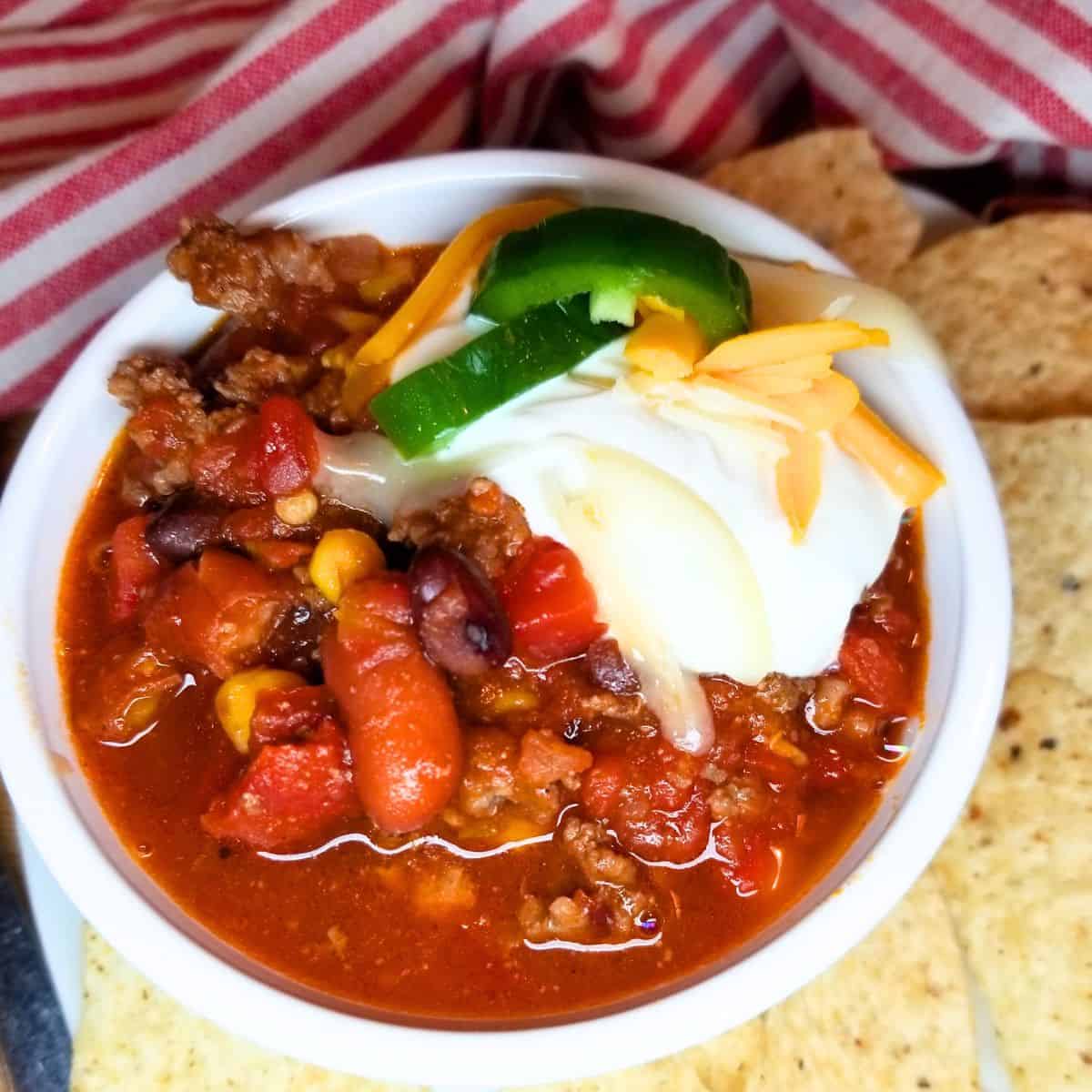 Taco soup in a bowl with sour cream, cheese, and jalapenos. Tortilla chips on the side.