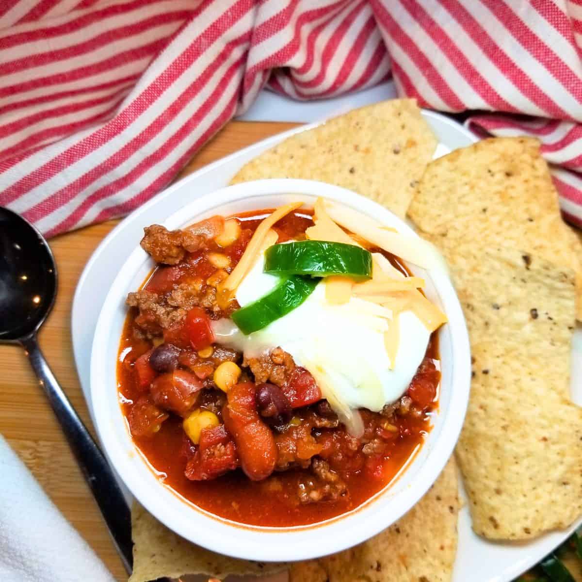 Taco soup in a bowl with sour cream, cheese, and jalapenos. Tortilla chips on the side.