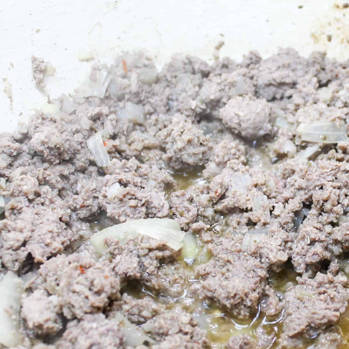 Browning beef and sausage with onion in a pan on the stovetop.