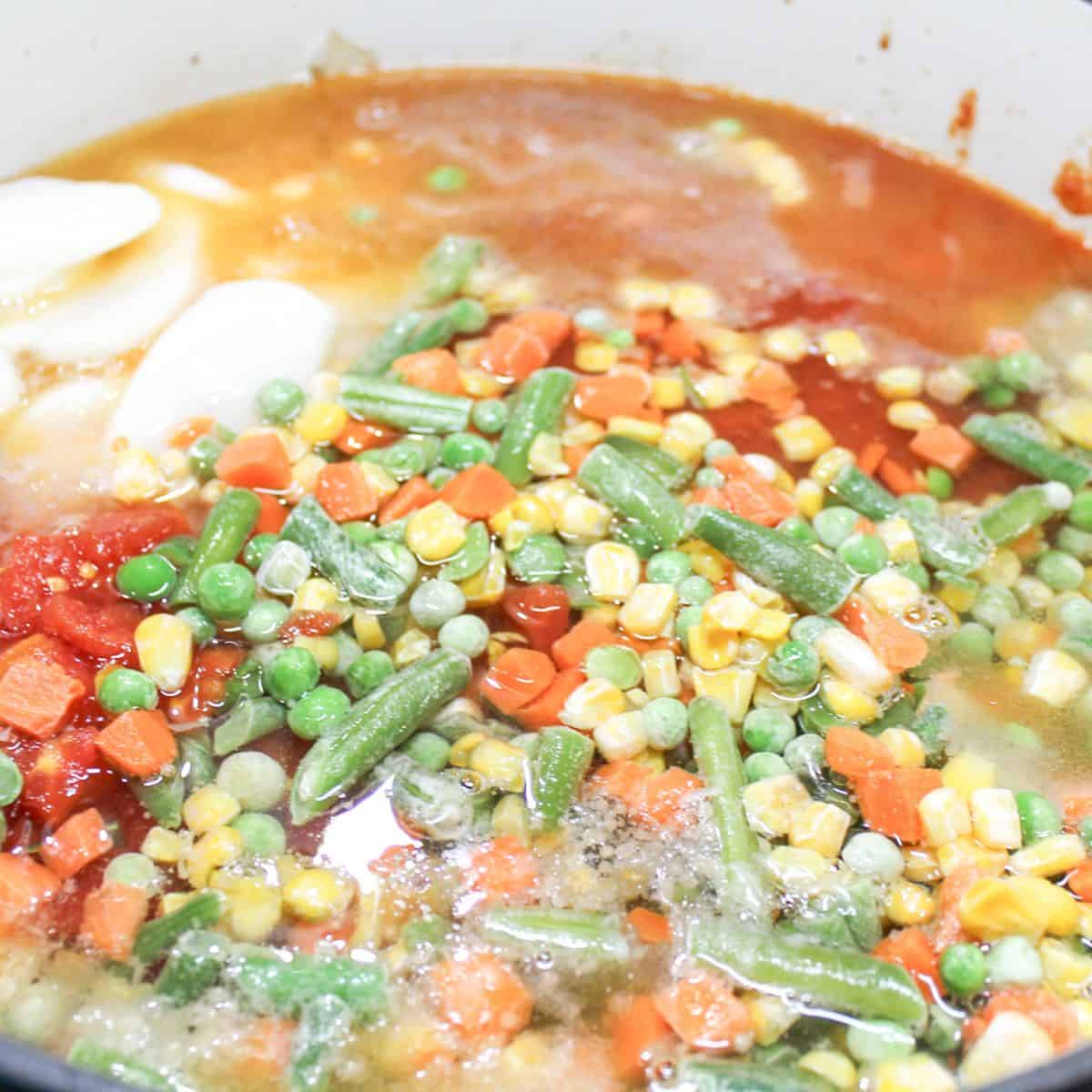 Adding ingredients to a large pot of vegetable soup.