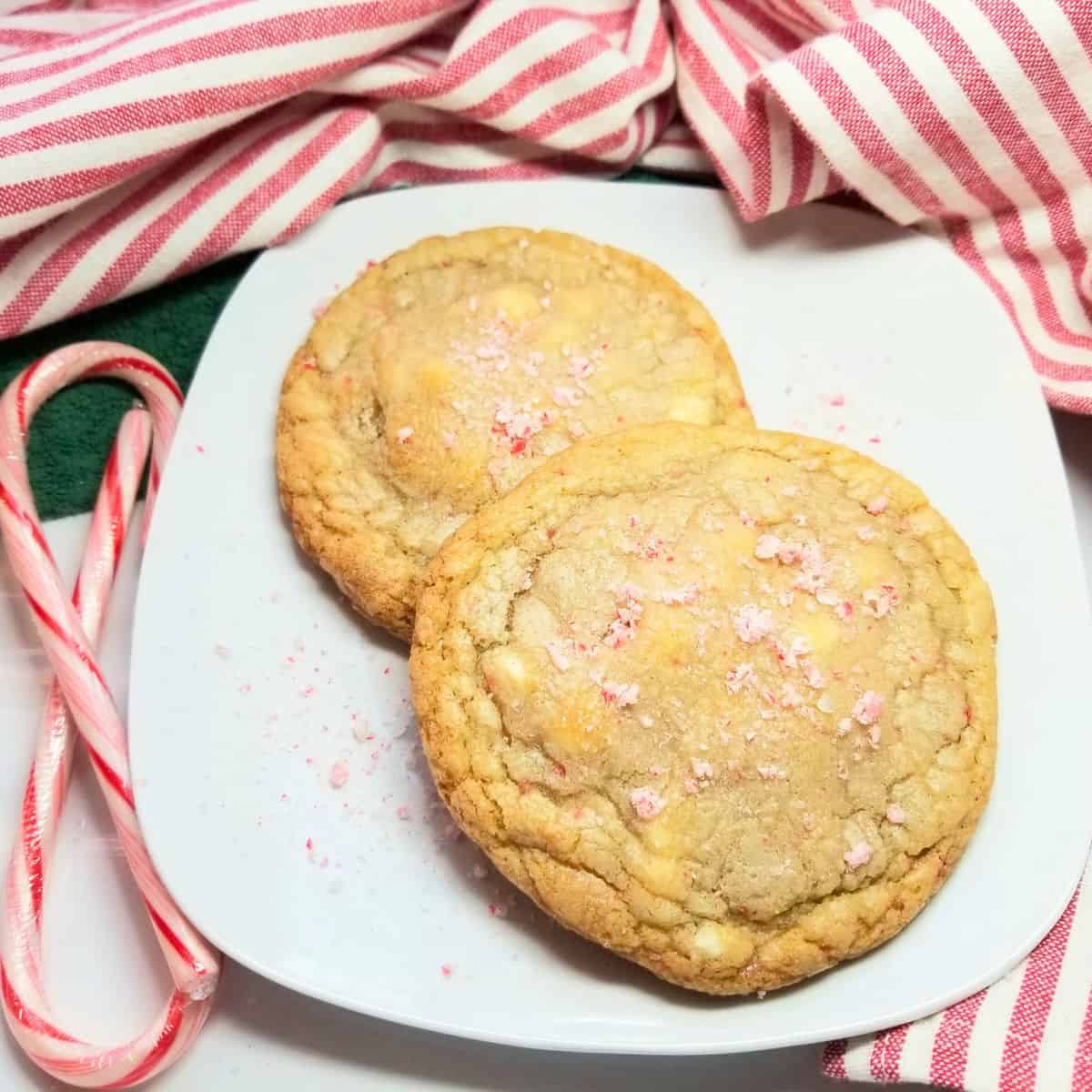 Baked white chocolate and peppermint cookies on a white plate with candy canes next to the plate and a green and stripped dish towel.