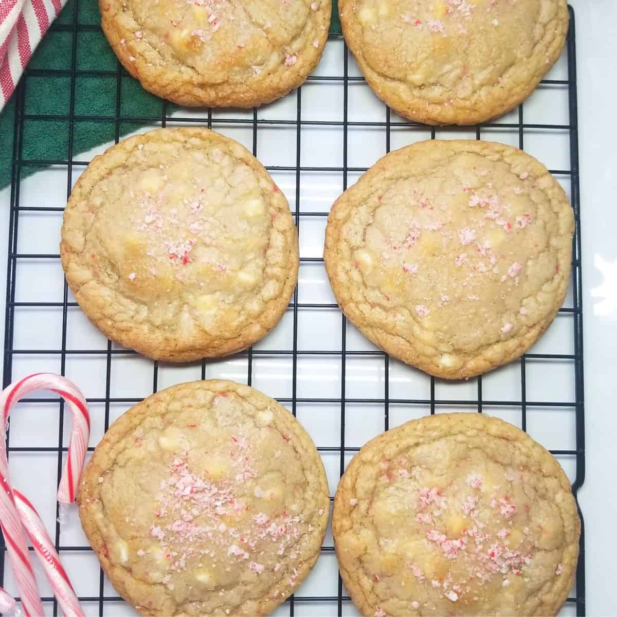 White chocolate peppermint cookies on a cooling rack with candy canes and a stripped dish towel.