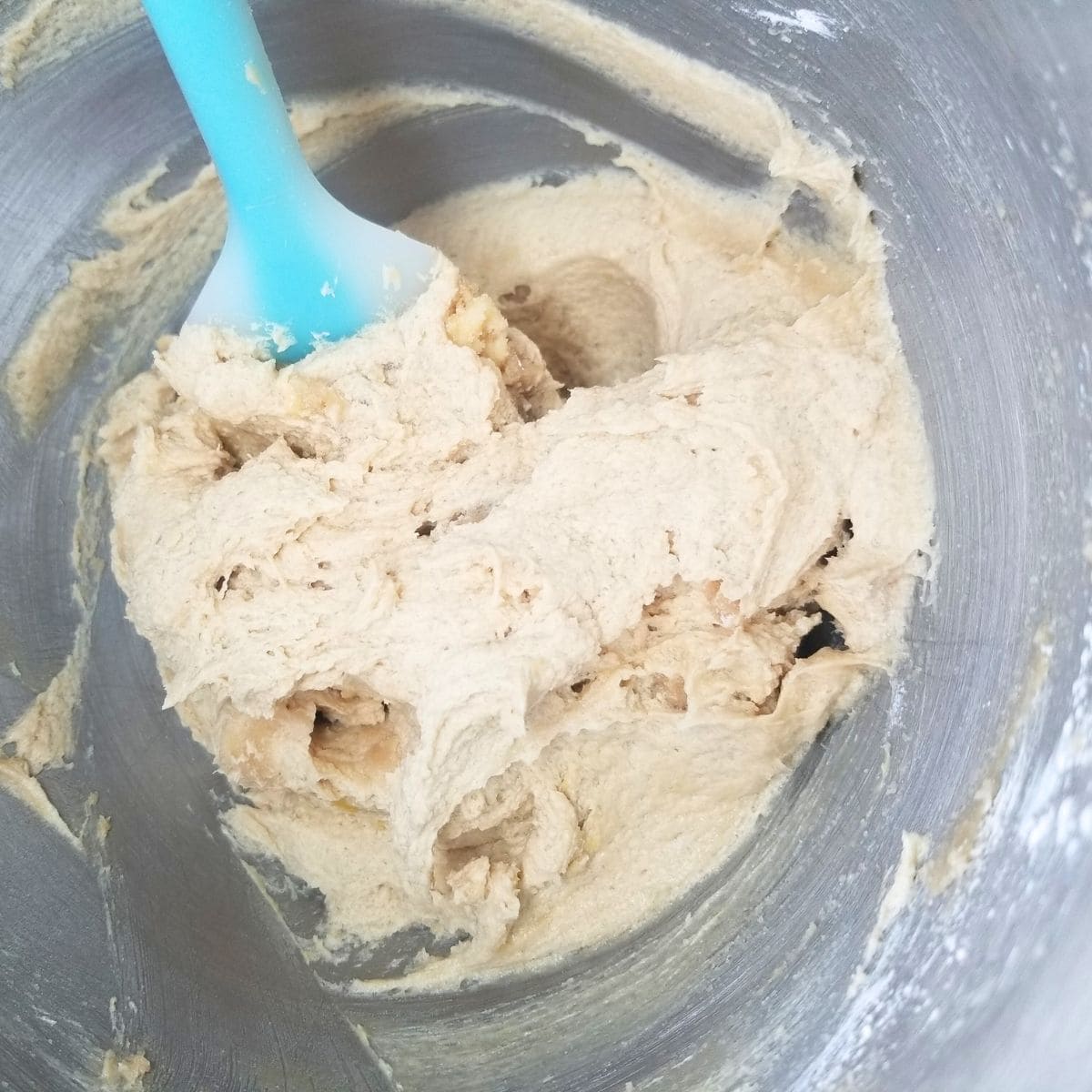 Creamed butter and sugars in a mixing bowl with a blue spatula.