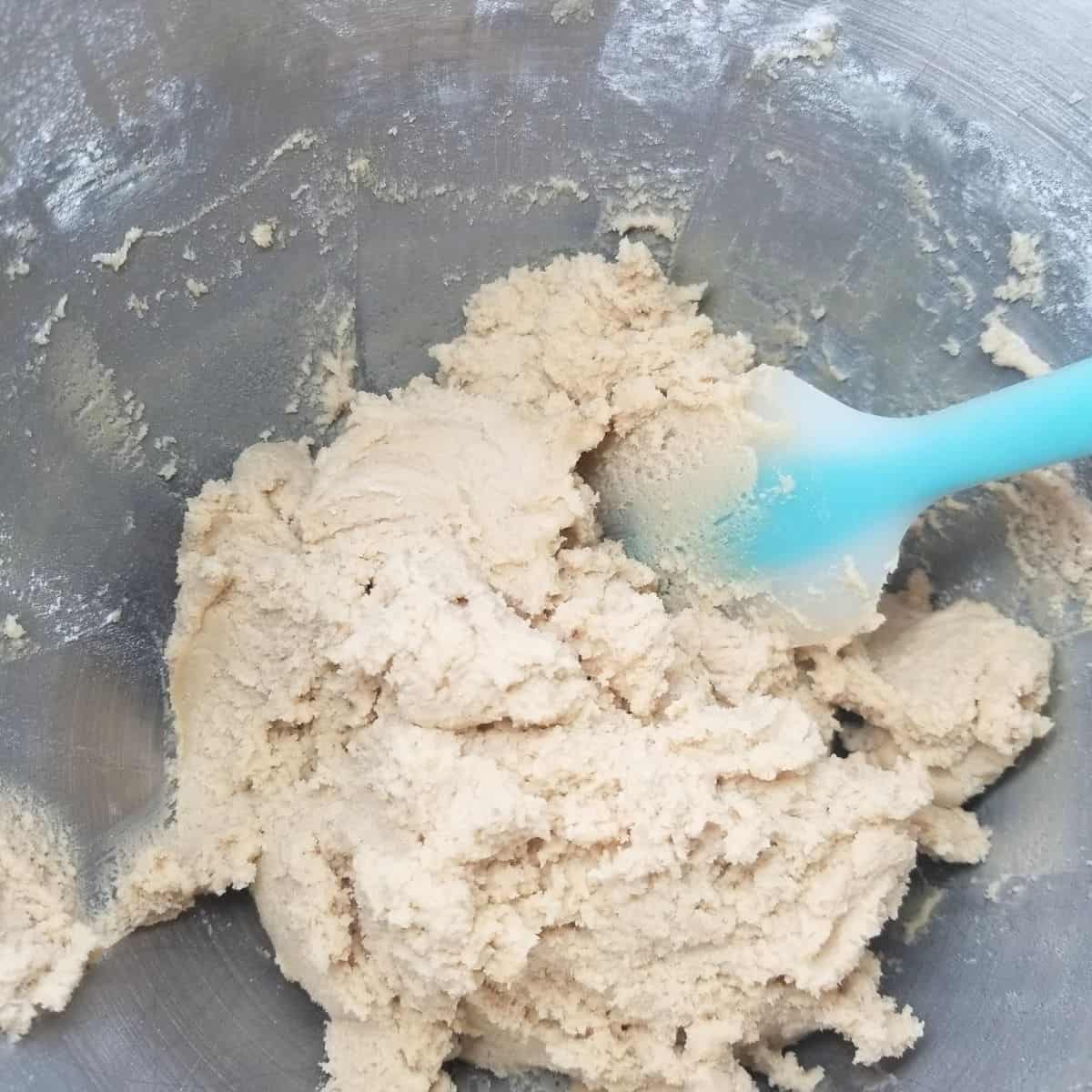 Cookie dough in a mixing bowl with a blue spatula.