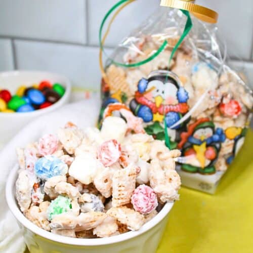 White trash snack mix in a white bowl and gift bag. M&M's in a white bowl sitting on a green dish towel.
