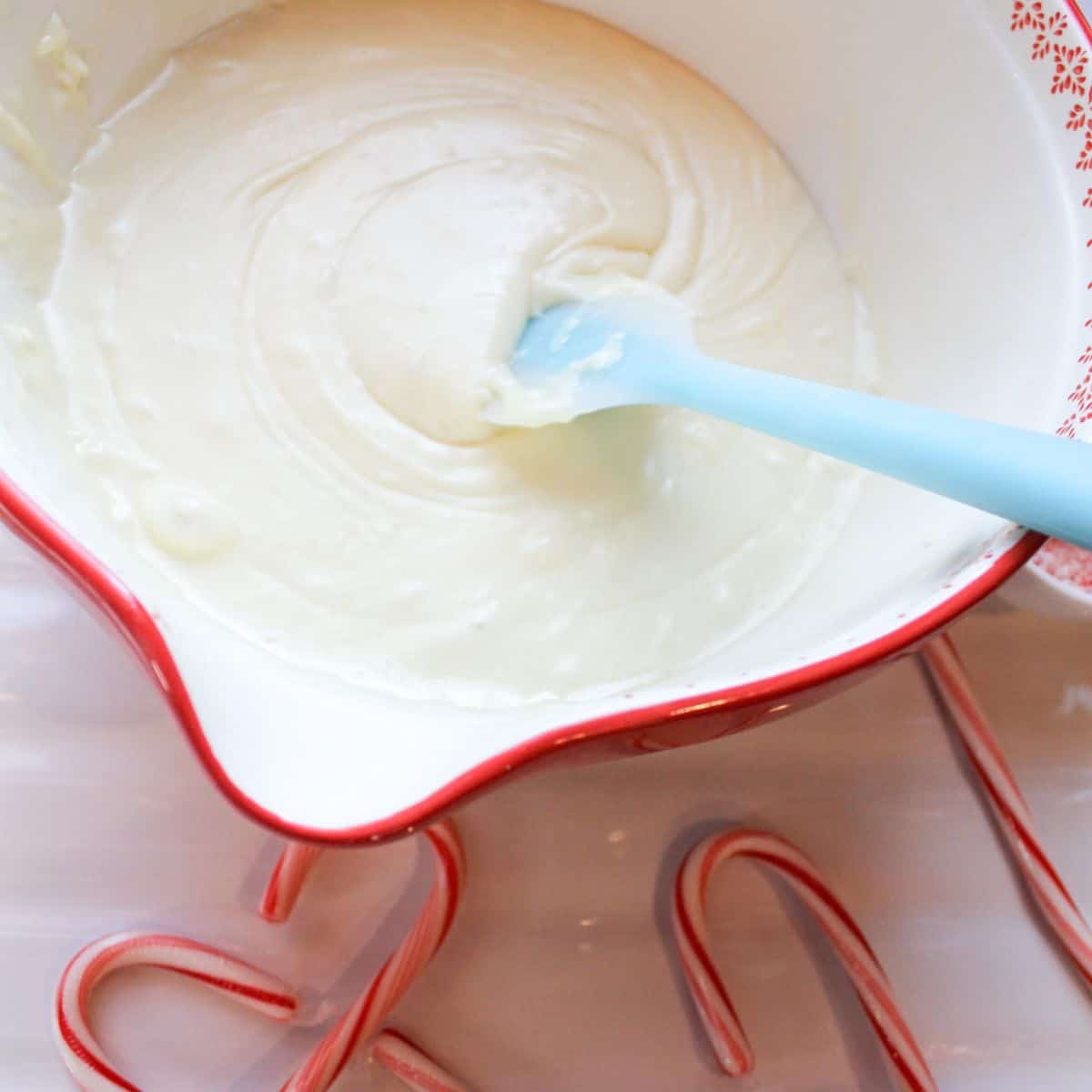 Melted chocolate in a red bowl with a blue spatula. Candy canes around the bowl.