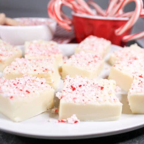 Peppermint fudge on a white plate with candy canes in a red bowl.