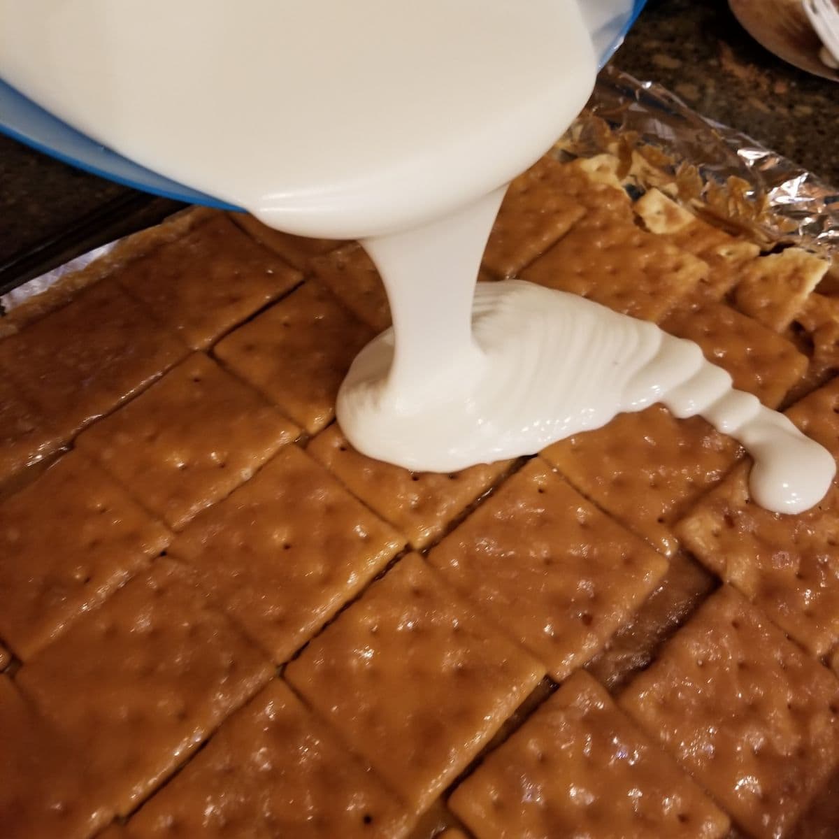 Pouring white chocolate over baked toffee on saltine crackers.