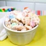 White Trash snack mix in a white bowl with a green cloth and M&Ms in a bowl.