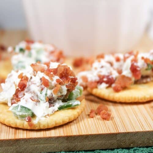 Cheese balls on crackers with bacon bits sitting on a wooden board.