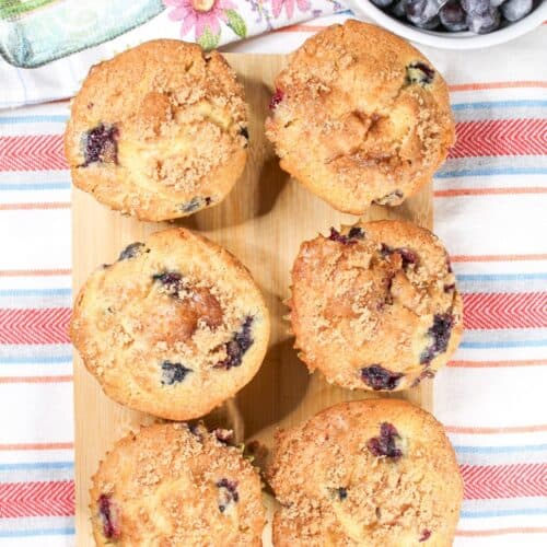 Blueberry muffins on a stripped dish towel with whole blueberries.