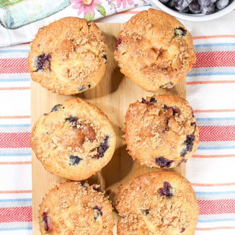 Blueberry muffins on a stripped dish towel with whole blueberries.