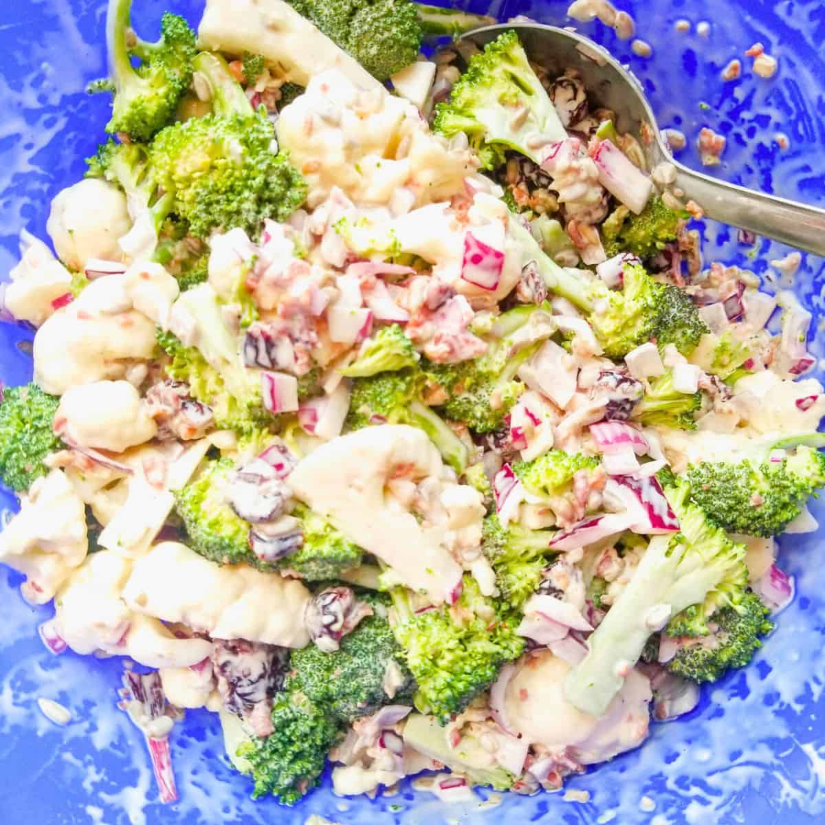 Mixed salad ingredients for broccoli cauliflower salad in a blue bowl.
