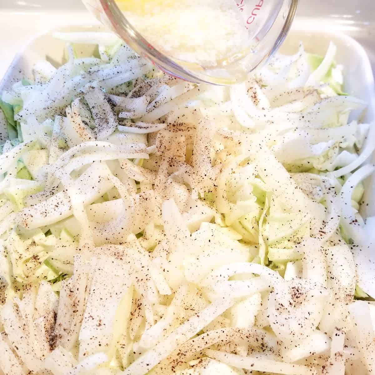 Chopped cabbage, sliced onions, salt, pepper, and melted butter in a baking dish.