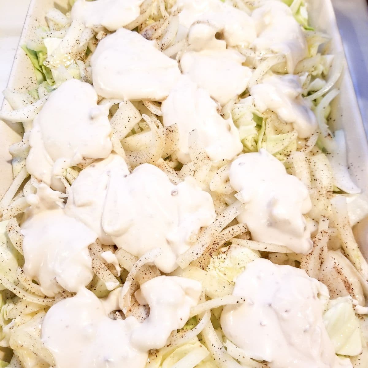 Cabbage casserole ingredients in a baking dish with cream of mushroom soup over the top.