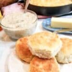 Biscuits on a plate and in a cast iron skillet with gravy in a bowl and a stick of butter in a dish.