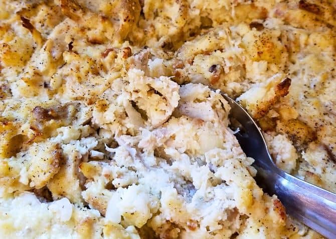 Cooked Chicken and Dressing in a dish with a serving spoon.