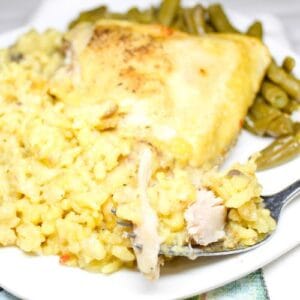 Chicken and yellow rice on a white plate with a fork and a side of green beans.