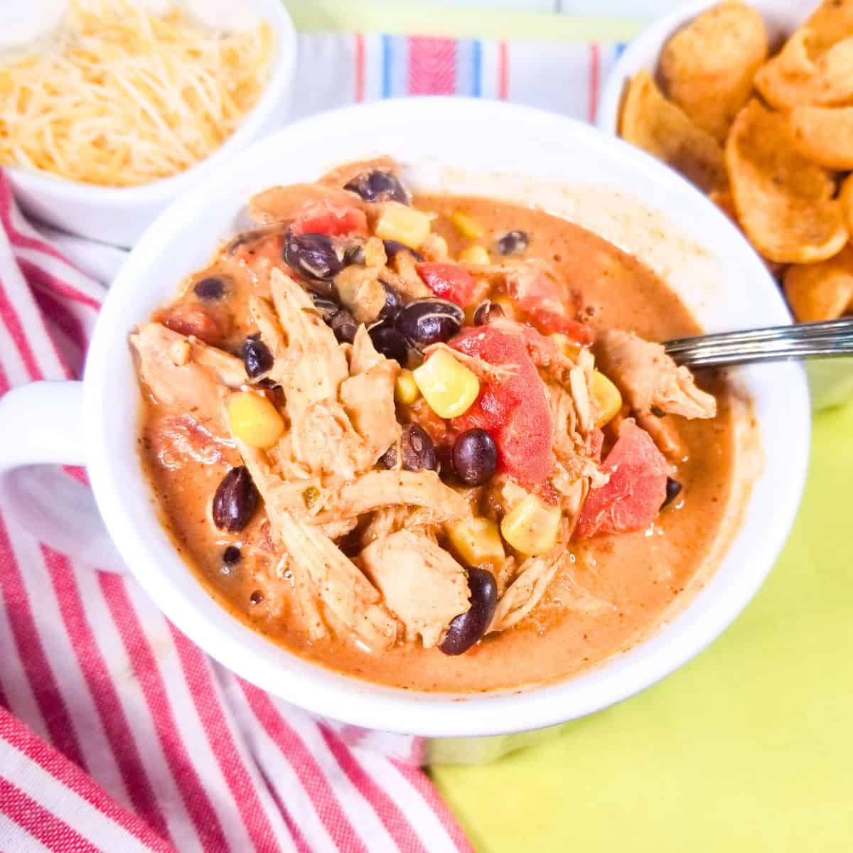 Cream cheese chicken chili served in a white mug with cheese and corn chips.