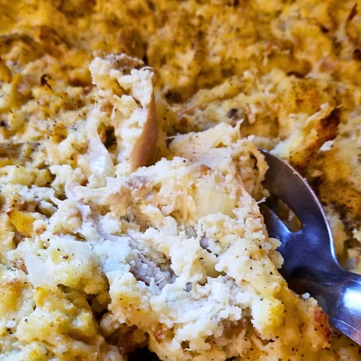 Cooked Southern Cornbread Dressing with Chicken in a serving bowl with a big spoon.