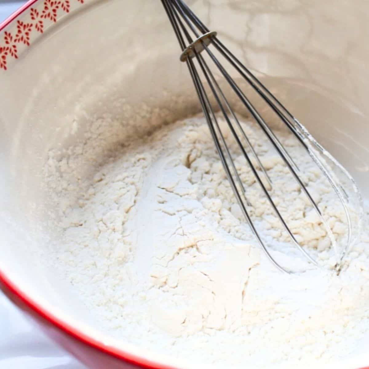 Flour mixture in a red bowl with a wire whisk.