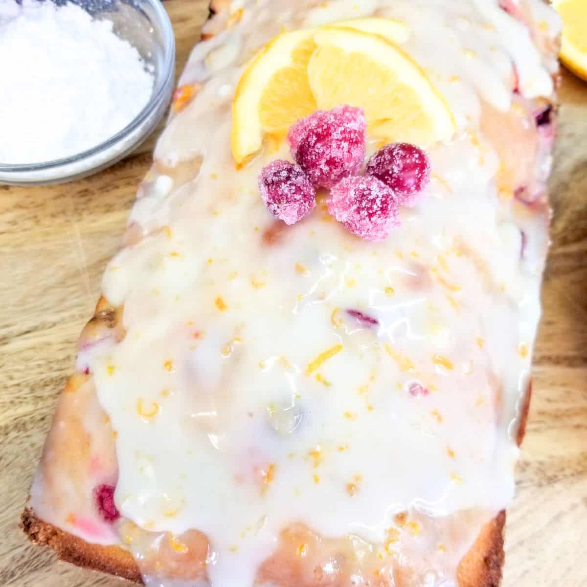Baked cranberry orange bread on a wooden tray with a bowl of powdered sugar.