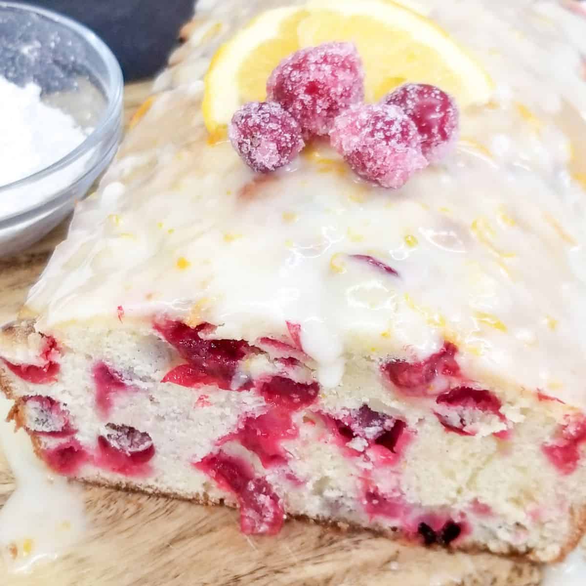 Cranberry Orange Bread on a wooden cutting board. Powdered sugar in a small bowl.