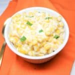 Cream corn in a white bowl with an orange dish cloth under the bowl.