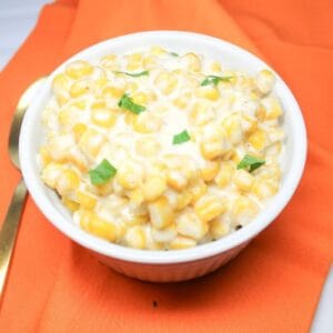 Cream corn in a white bowl with an orange dish cloth under the bowl.