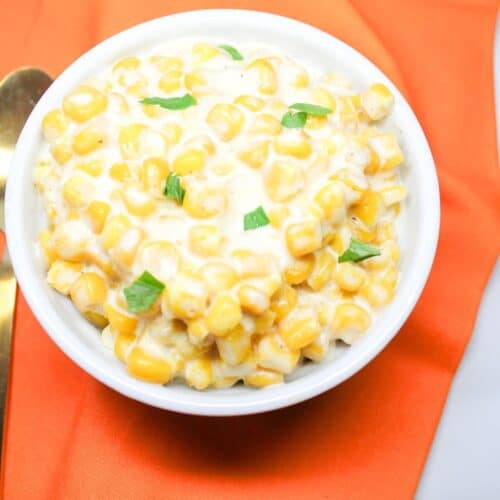 Crock pot creamed corn in a white bowl sitting on an orange napkin.