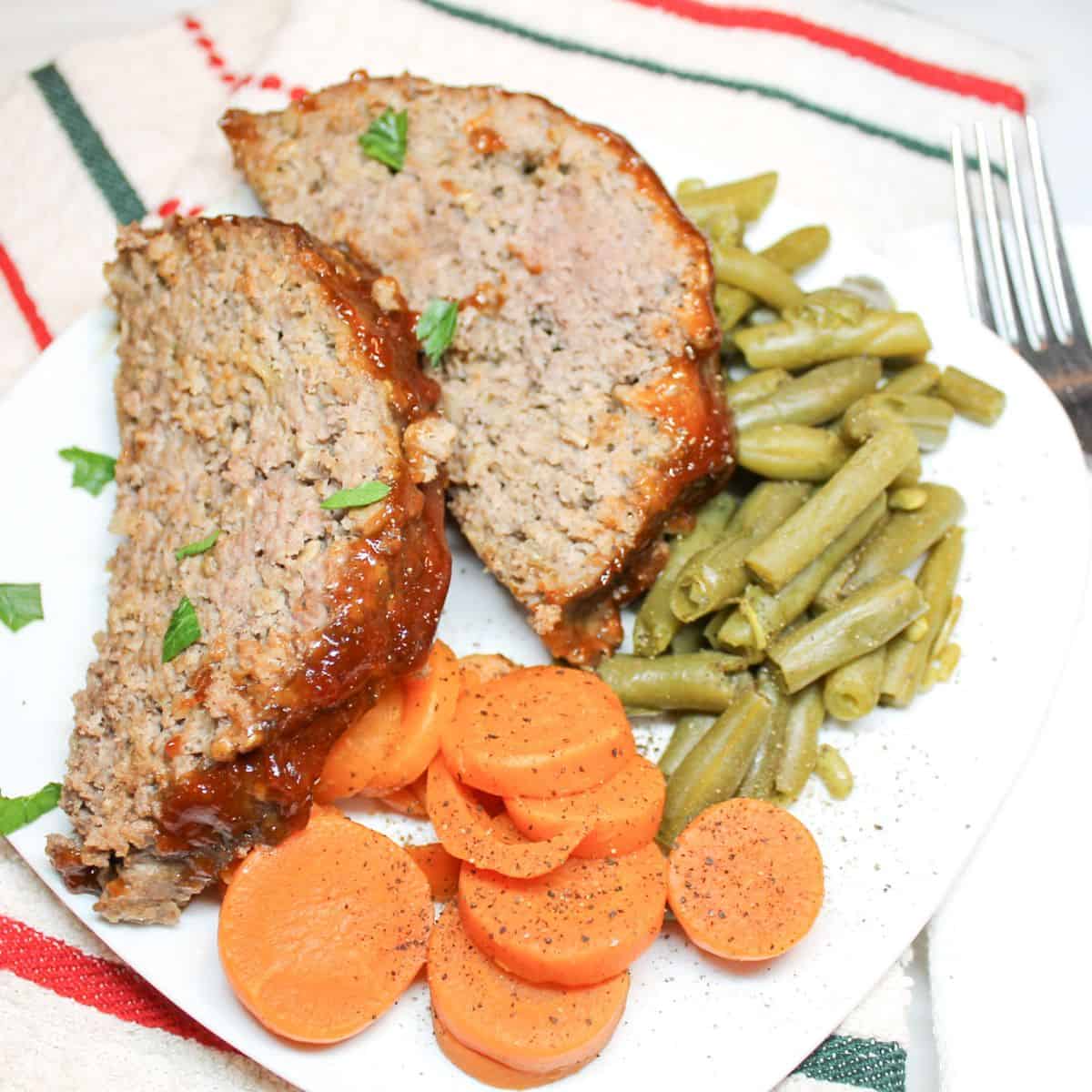 Meatloaf with a side of carrots and green beans on a white plate.